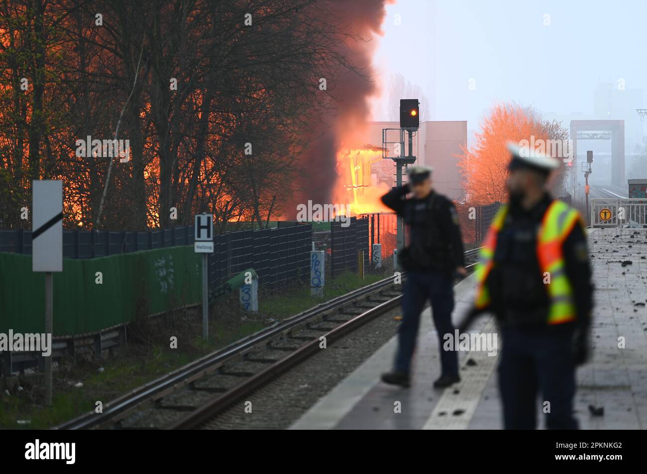 Hamburg, Deutschland. 09. April 2023. Polizeibeamte gehen entlang der Gleise des Bahnhofs Hamburg-Rothenburgsort, während im Hintergrund Flammen eines Großbrands zu sehen sind. Aufgrund der starken Rauch- und Gasentwicklung mit möglichen chemischen Komponenten hat die örtliche Polizei eine offizielle Gefahrenwarnung ausgegeben. Kredit: Jonas Walzberg/dpa/Alamy Live News Stockfoto