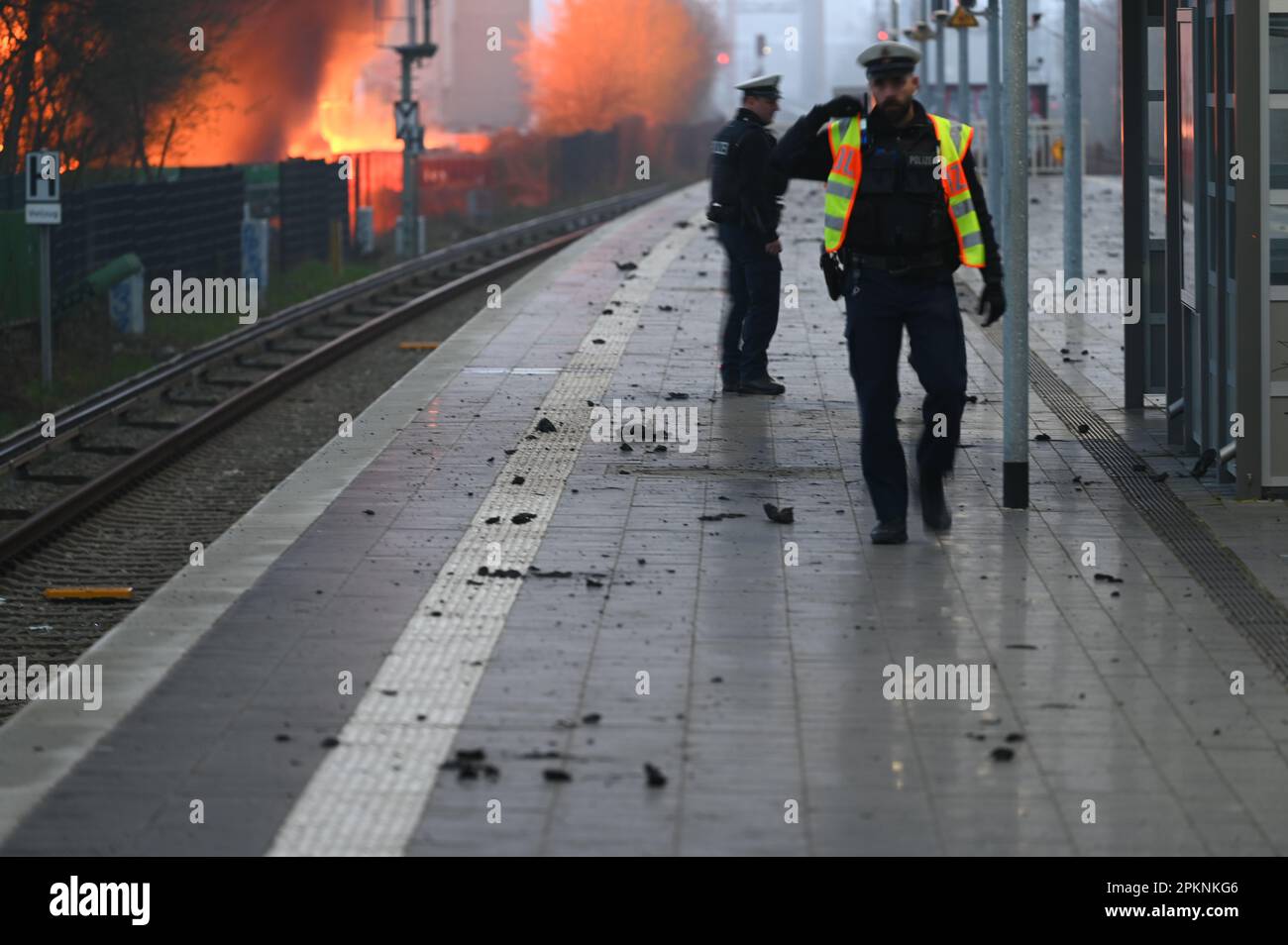 Hamburg, Deutschland. 09. April 2023. Polizeibeamte gehen entlang der Gleise des Bahnhofs Hamburg-Rothenburgsort, während im Hintergrund Flammen eines Großbrands zu sehen sind. Aufgrund der starken Rauch- und Gasentwicklung mit möglichen chemischen Komponenten hat die örtliche Polizei eine offizielle Gefahrenwarnung ausgegeben. Kredit: Jonas Walzberg/dpa/Alamy Live News Stockfoto