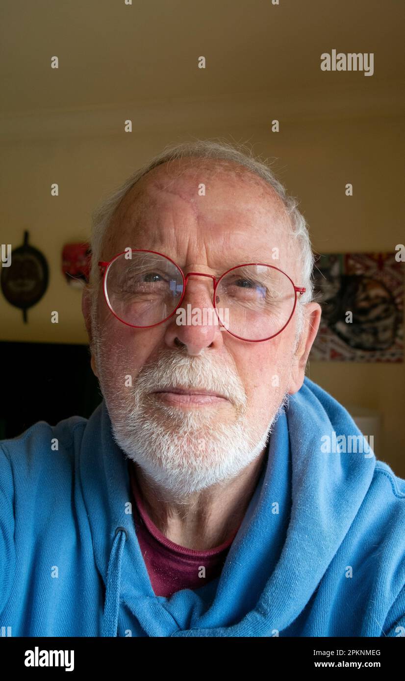 Ein 80-jähriger Mann, ein Rentner mit grauem Bart und roter Brille und blauem Kapuzenpullover Stockfoto