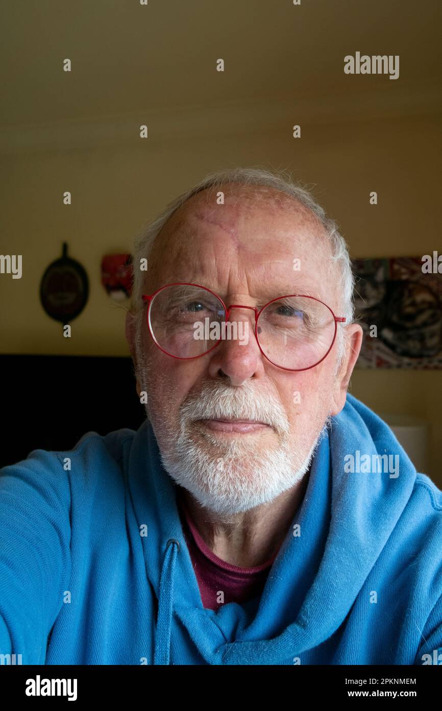 Ein 80-jähriger Mann, ein Rentner mit grauem Bart und roter Brille und blauem Kapuzenpullover Stockfoto