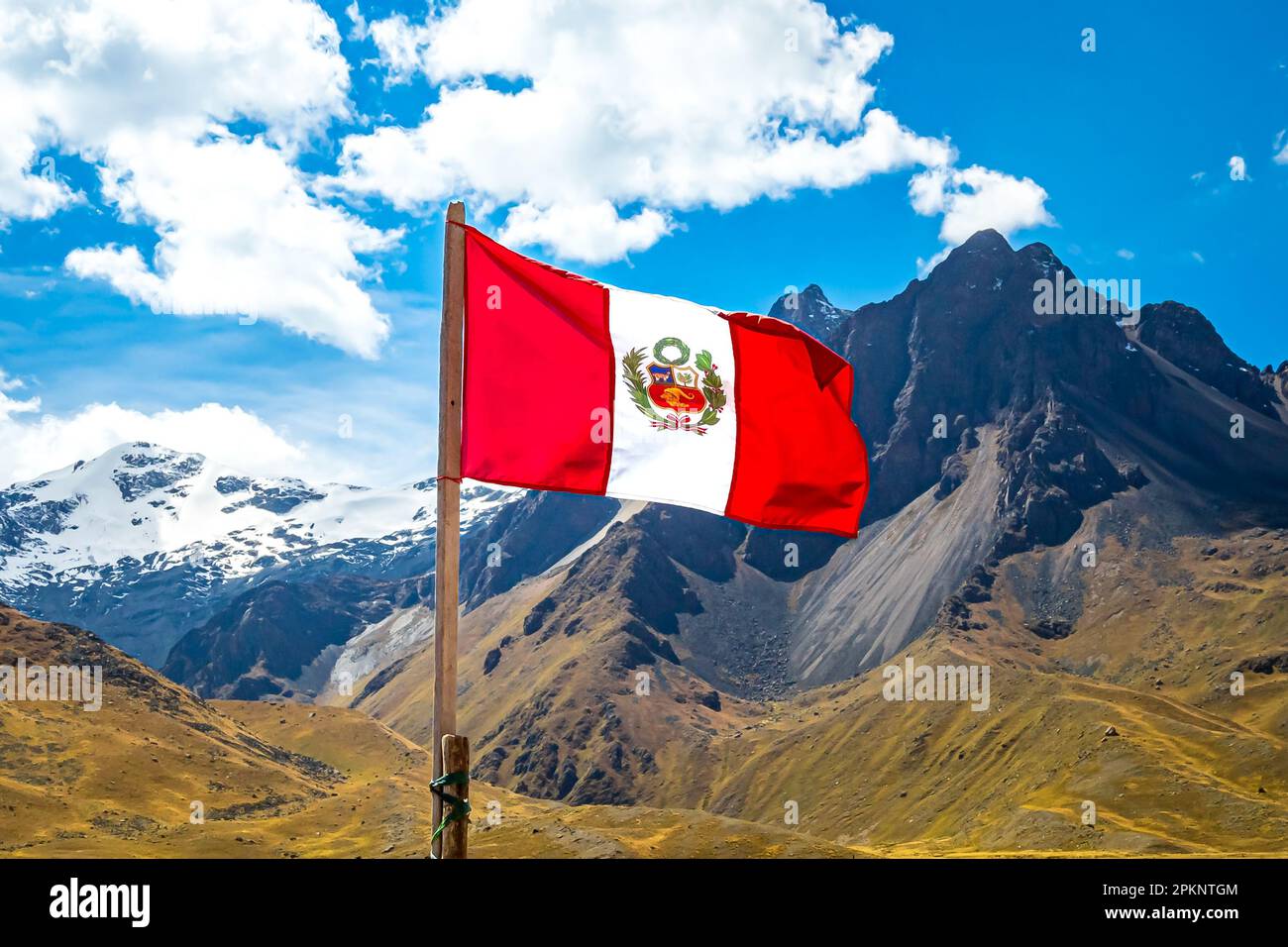 Die peruanische Flagge flattert im Wind vor dem majestätischen Gebirge La Raya mit dem schneebedeckten Gipfel von Chimboya im Hintergrund. Stockfoto