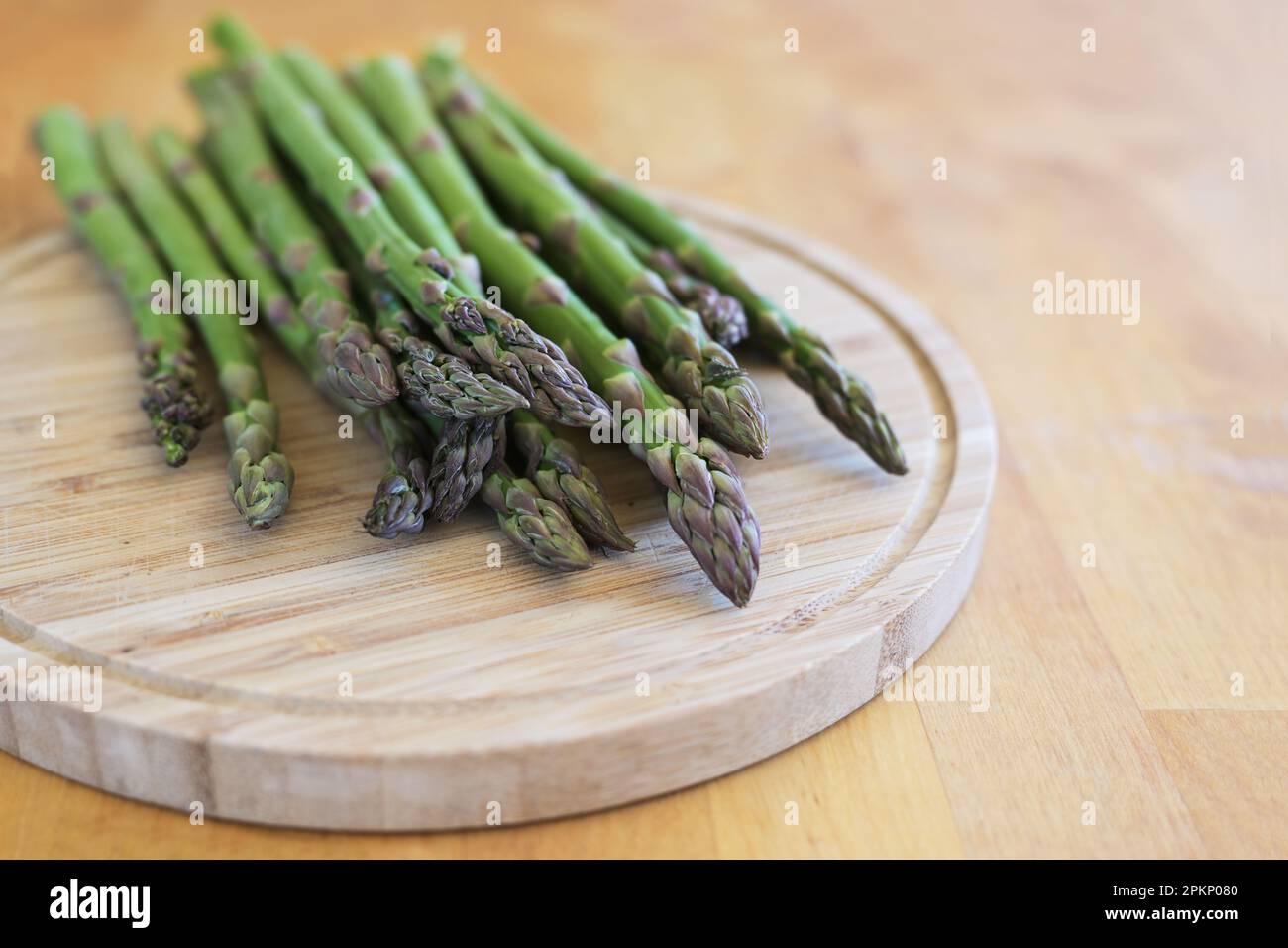 Frischer grüner Spargel auf einem Schneidebrett und einem Holztisch, köstliches Frühlingsgemüse, Kopierraum, ausgewählter Fokus, schmale Schärfentiefe Stockfoto