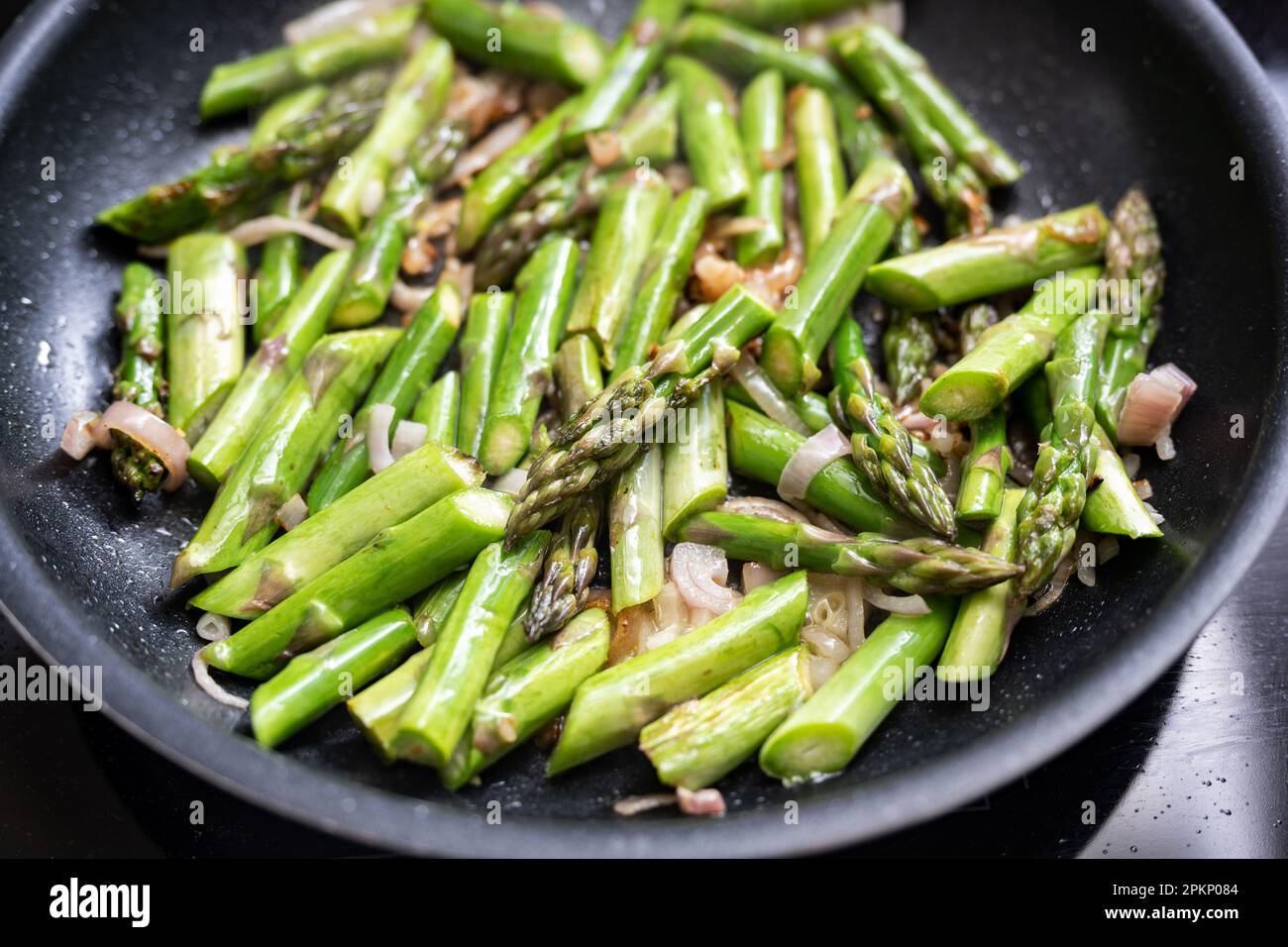 Grüne Spargelstücke mit Zwiebeln in einer schwarzen Bratpfanne, Kochkonzept für vegetarisches Gemüsemehl mit Frühlingsgemüse, ausgewählter Fokus, na Stockfoto