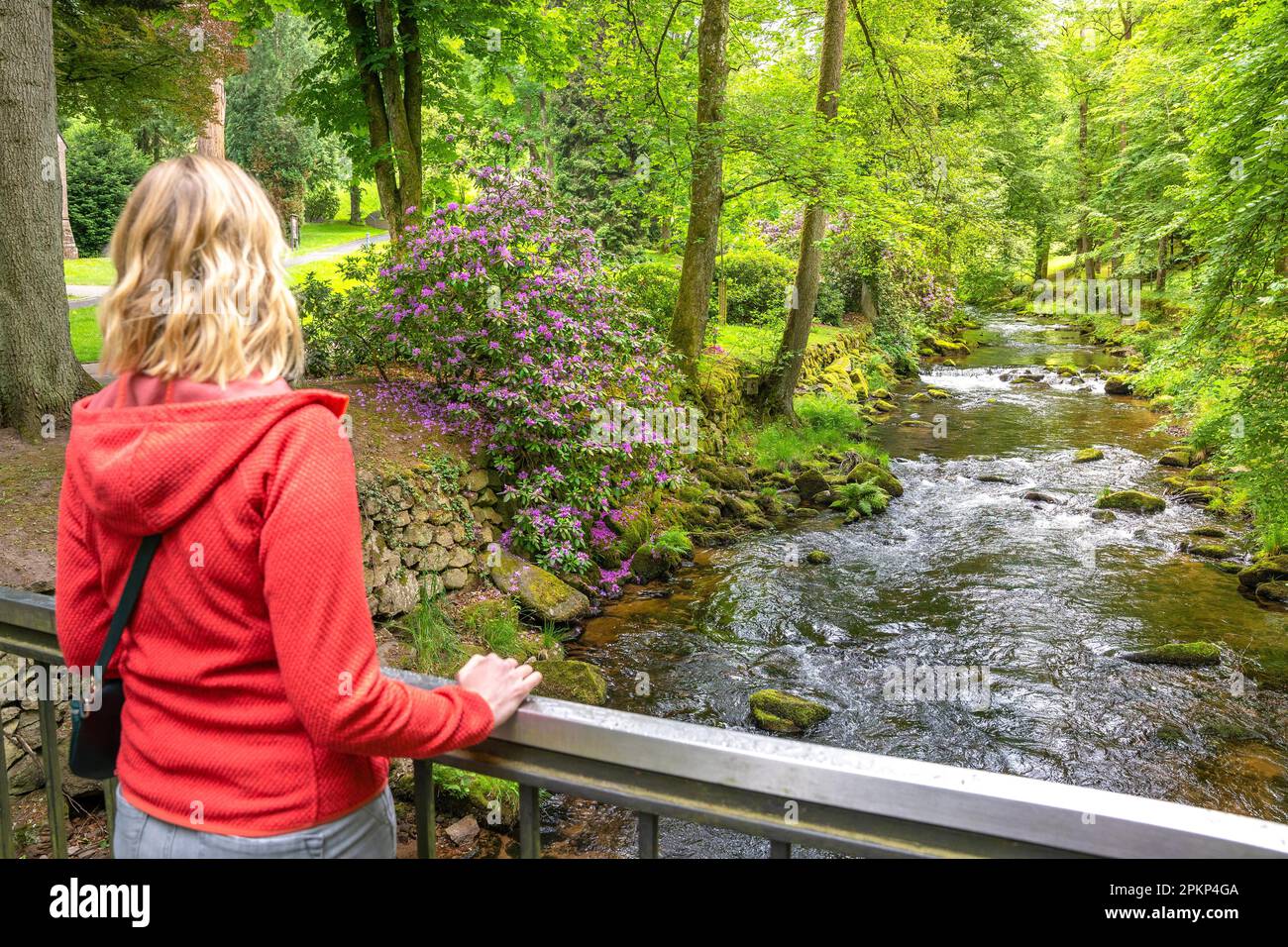 Eine Frau, die auf einer Brücke steht und die blühenden Kurgärten und den Fluss ansieht, Bad Wildbad, Schwarzwald, Deutschland, Europa Stockfoto