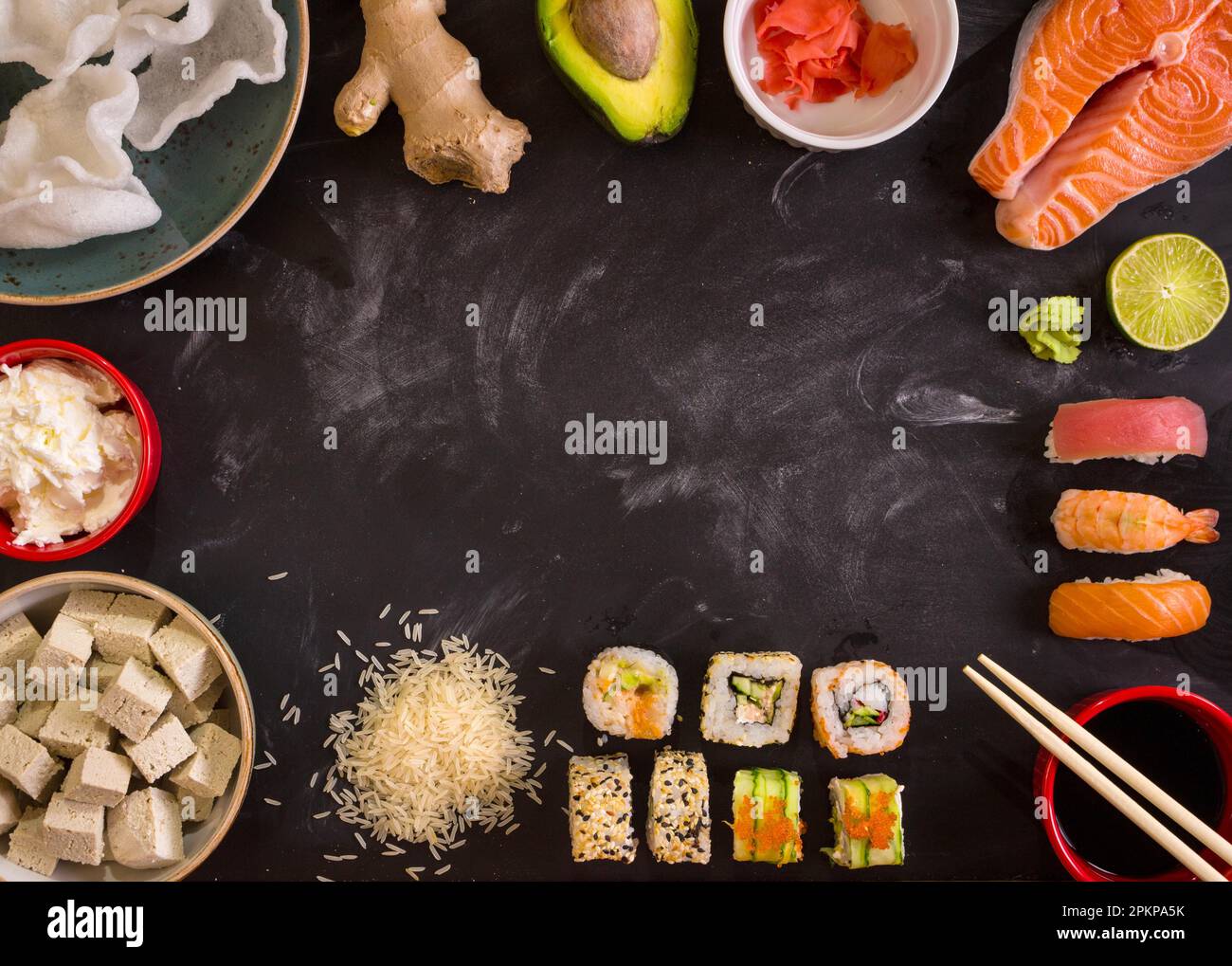 Aufnahme von Sushi und Zutaten über Kopf auf dunklem Hintergrund. Sushi Brötchen, Nigiri, rohes Lachssteak, Reis, Frischkäse, Avocado, Limette, eingelegter Ingwer (g Stockfoto