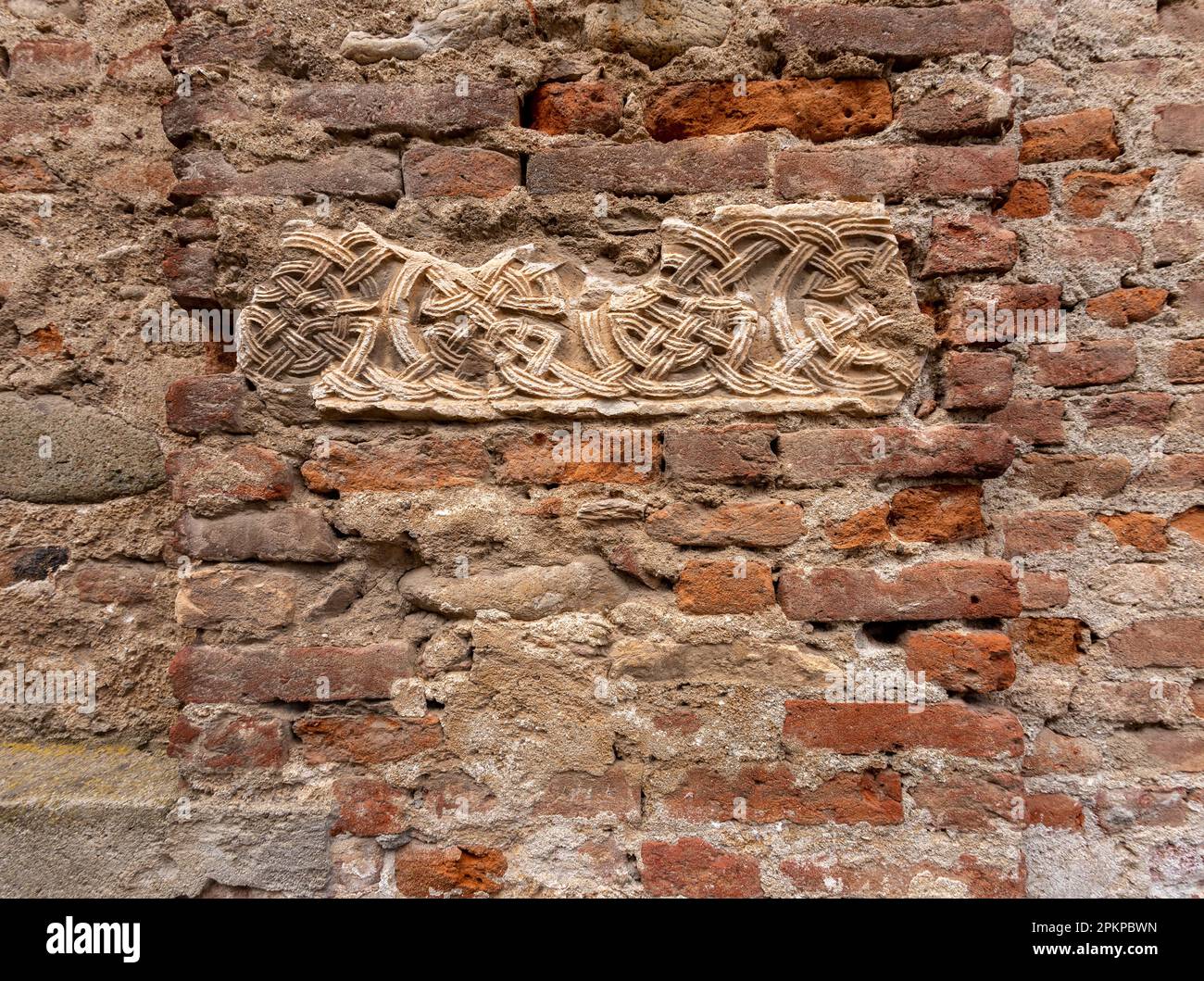 Textur der antiken Mauer mit Stücken aus alten roten Ziegeln gemischt mit freiliegenden runden Flusssteinen und Einlage aus mittelalterlich dekoriertem Stein Stockfoto