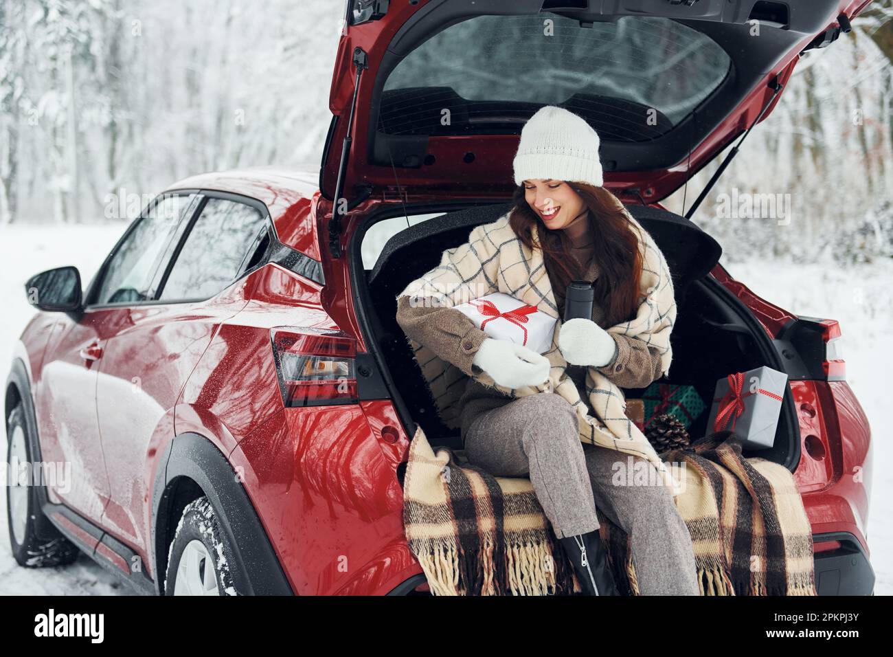 Weihnachtsgeschenke. Schöne junge Frau ist im Winter in der Nähe ihres roten Autos Stockfoto