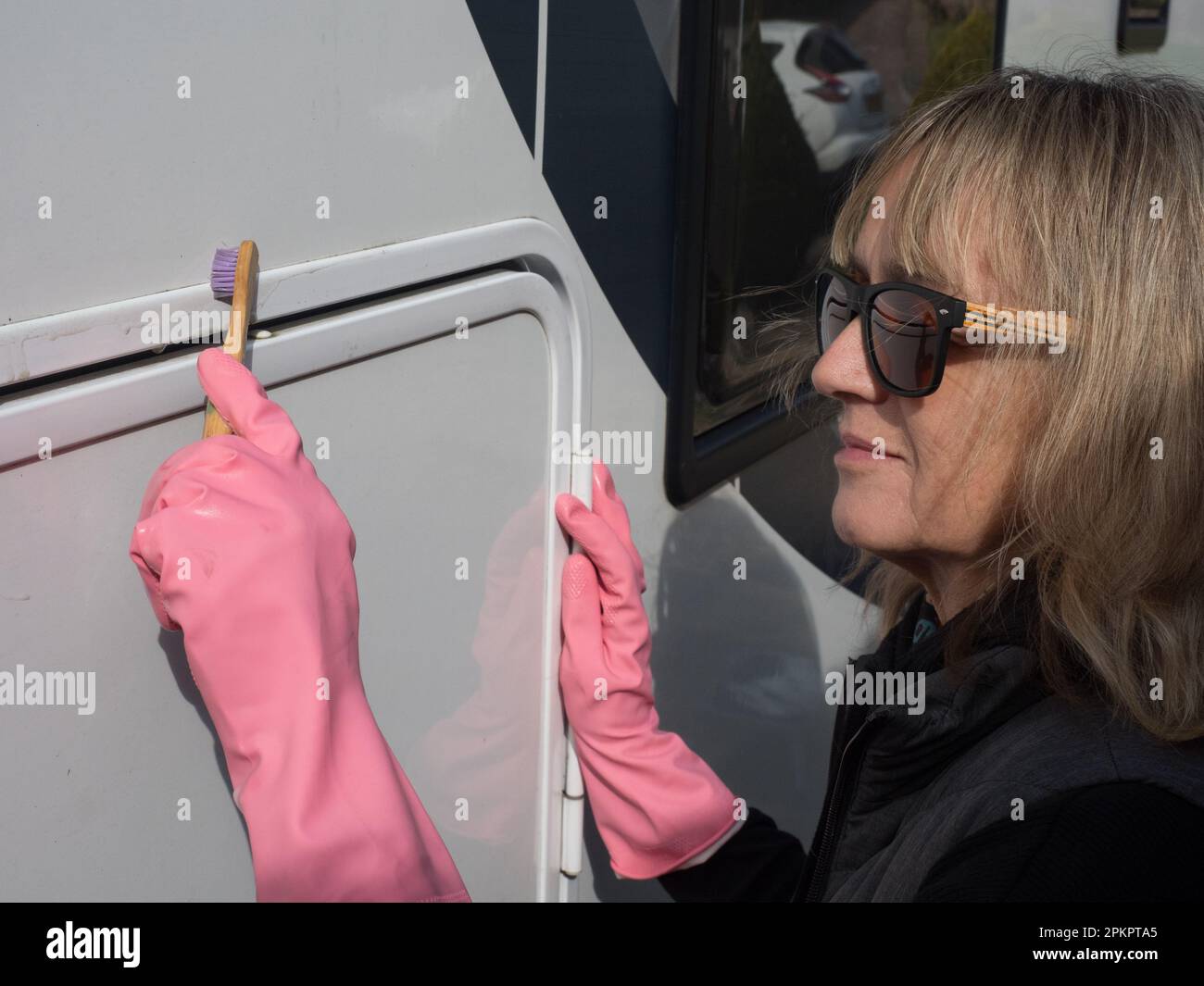 Eine attraktive weibliche Hand reinigt ihr Wohnmobil mit einer Zahnbürste. Sie trägt pinkfarbene Gummihandschuhe und eine Sonnenbrille. Zufrieden Stockfoto