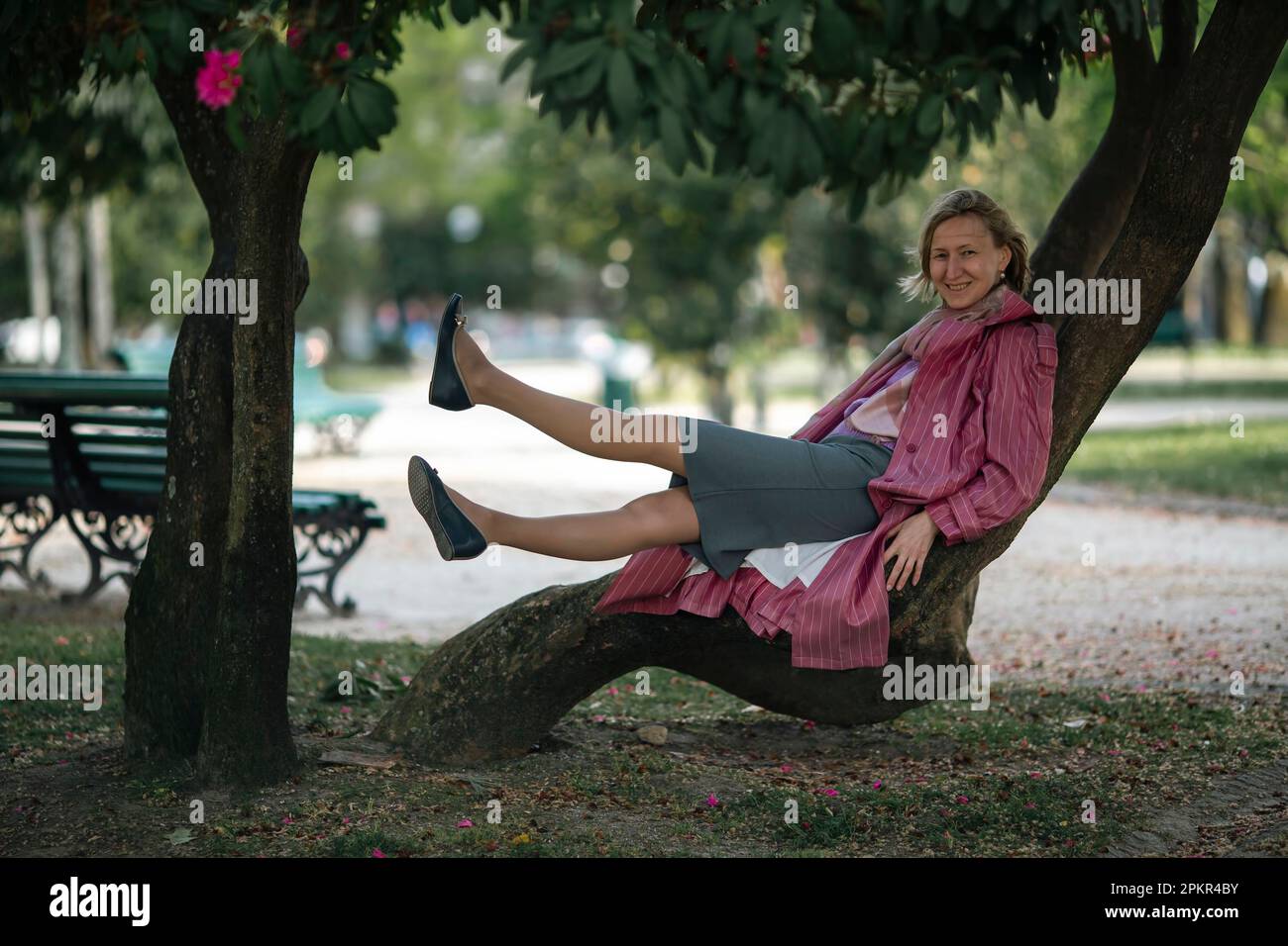 Eine Frau in einem rosa Regenmantel im Stil der 80s Posen im Park. Stockfoto