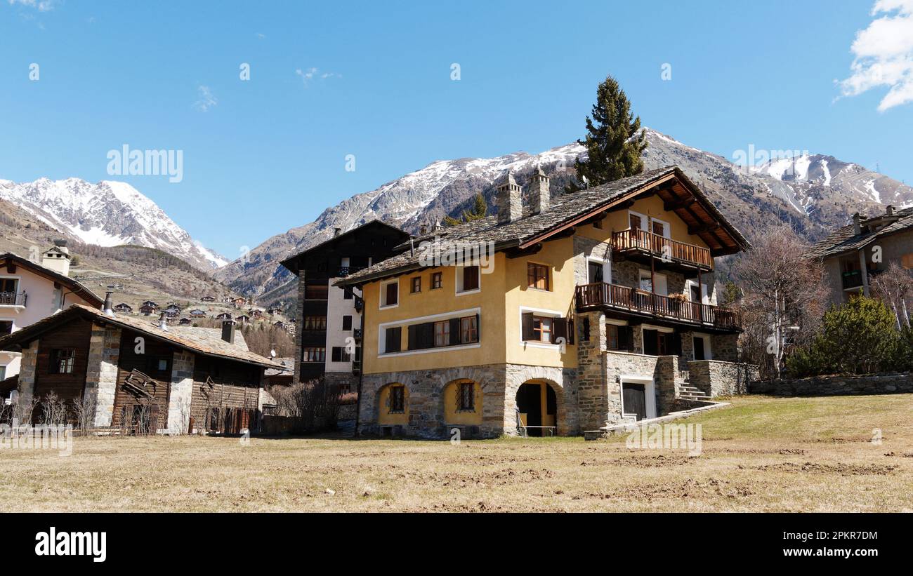Großes gelbes Hotel mit Balkon und einem Berg in Cogne, Hauptstadt des Gran Paradiso Nationalparks in der Region Aosta Valley, Italien Stockfoto