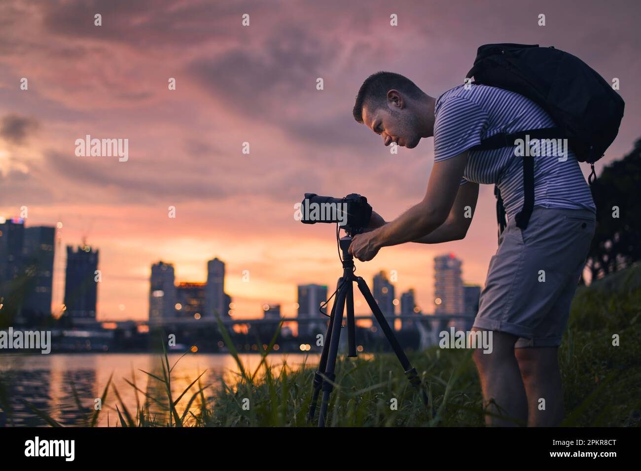 Konzentrierter Fotograf mit Kamera auf dem Stativ, während er Fotos von der Skyline der Stadt macht. Moderne Stadt bei schönem Sonnenuntergang, Singapur. Stockfoto