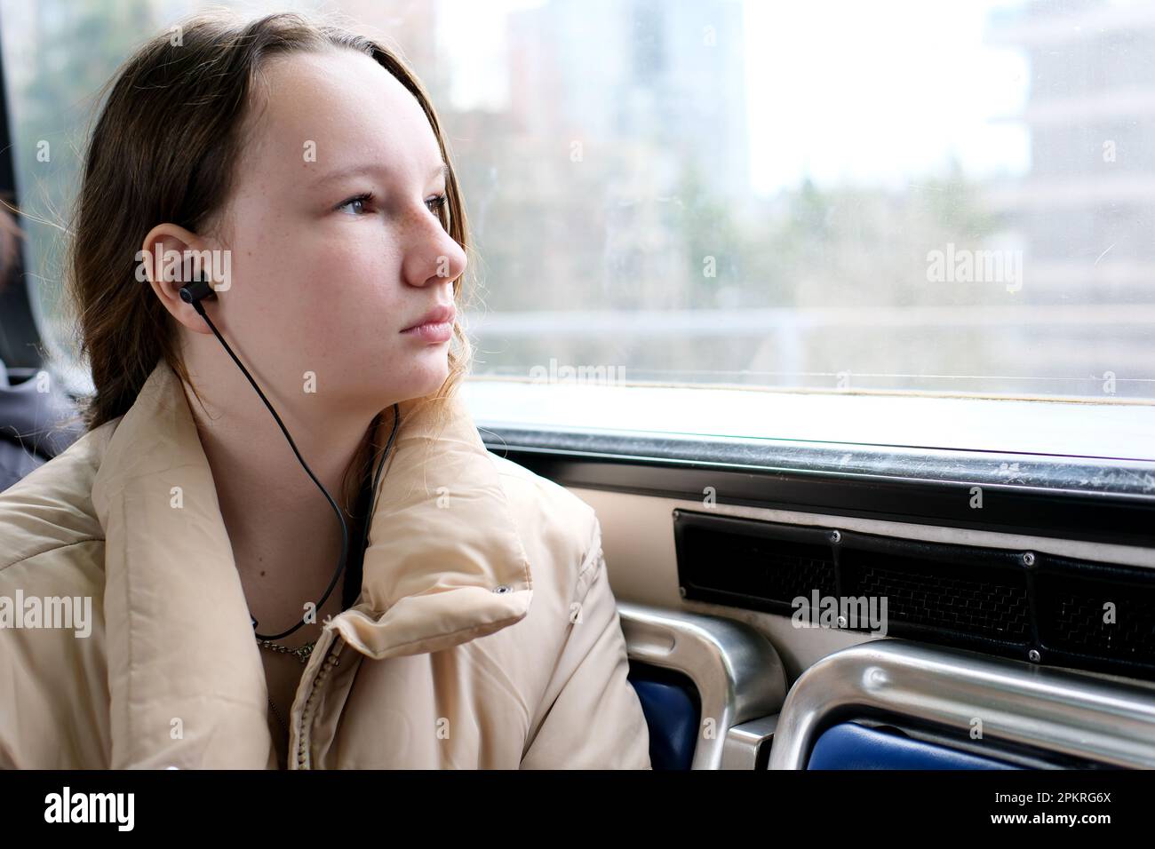 Junge Teenager, die im Transport mitfährt, schaut aus dem Fenster Kopfhörer Mobiltelefon friedliche Gesichtsfläche für Text Sky Train Bus Auto gewöhnliche Person in echten Straßen Städte kanada Vorort surrey Stockfoto