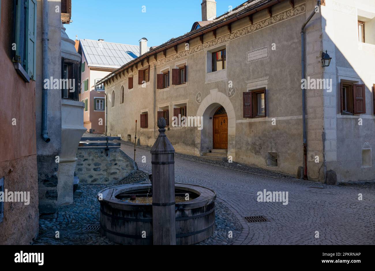 Dorf Guarda (1.653 m), Niederengadin, Graubünden, Schweiz: Alte Häuser (eines mit Inschrift) und Brunnen entlang der Chasa, der Hauptkopfsteingepflasterstraße Stockfoto