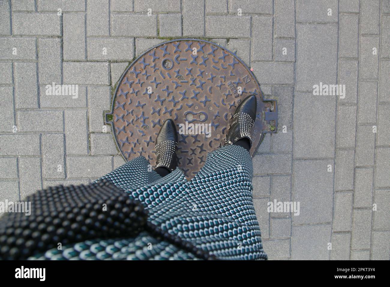 Frau in gemustertem Rock und schwarzen Cowboystiefeln mit Nieten auf der Kopfsteinpflasterstraße, Draufsicht Stockfoto
