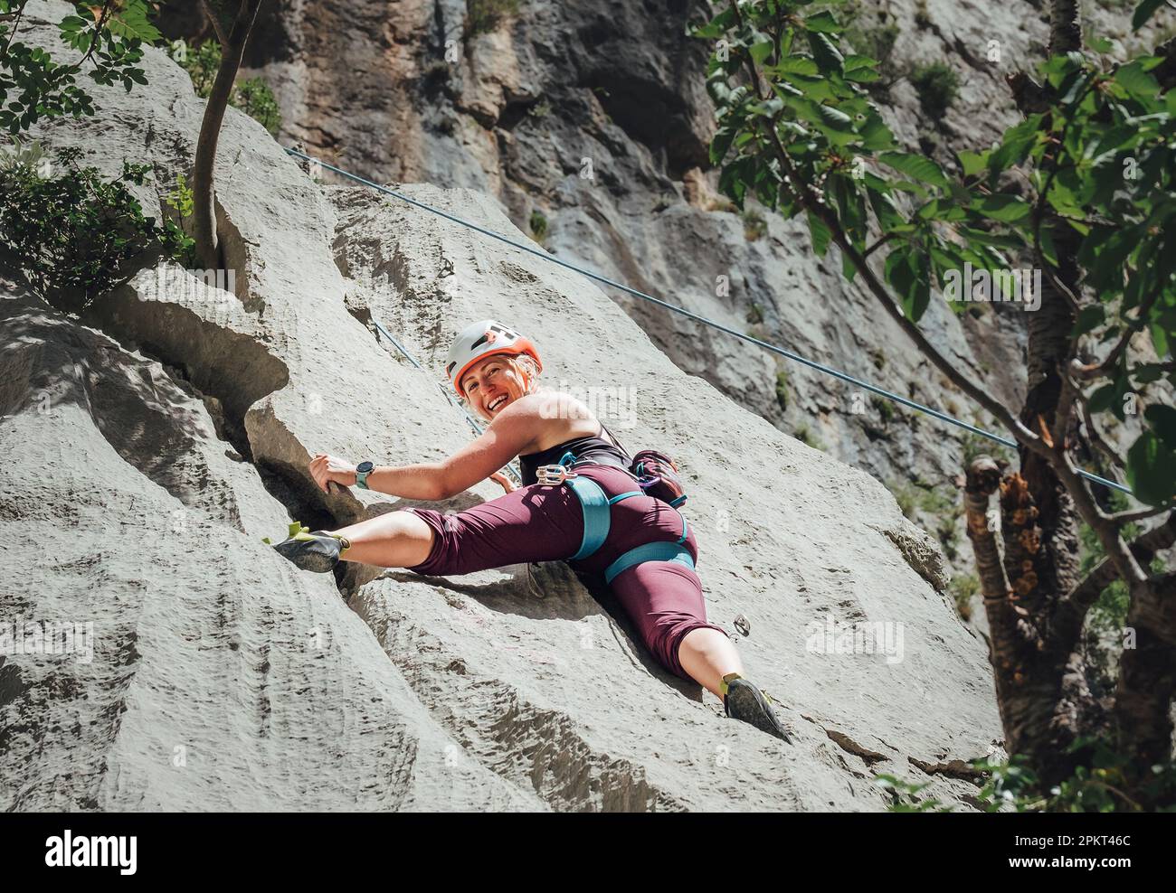 Lächelnde athletische Frau in Schutzhelm Klettern Klippe Felswand mit Top-Seil und Klettergurt in Paklenica Nationalpark-Website in Kroatien. A Stockfoto
