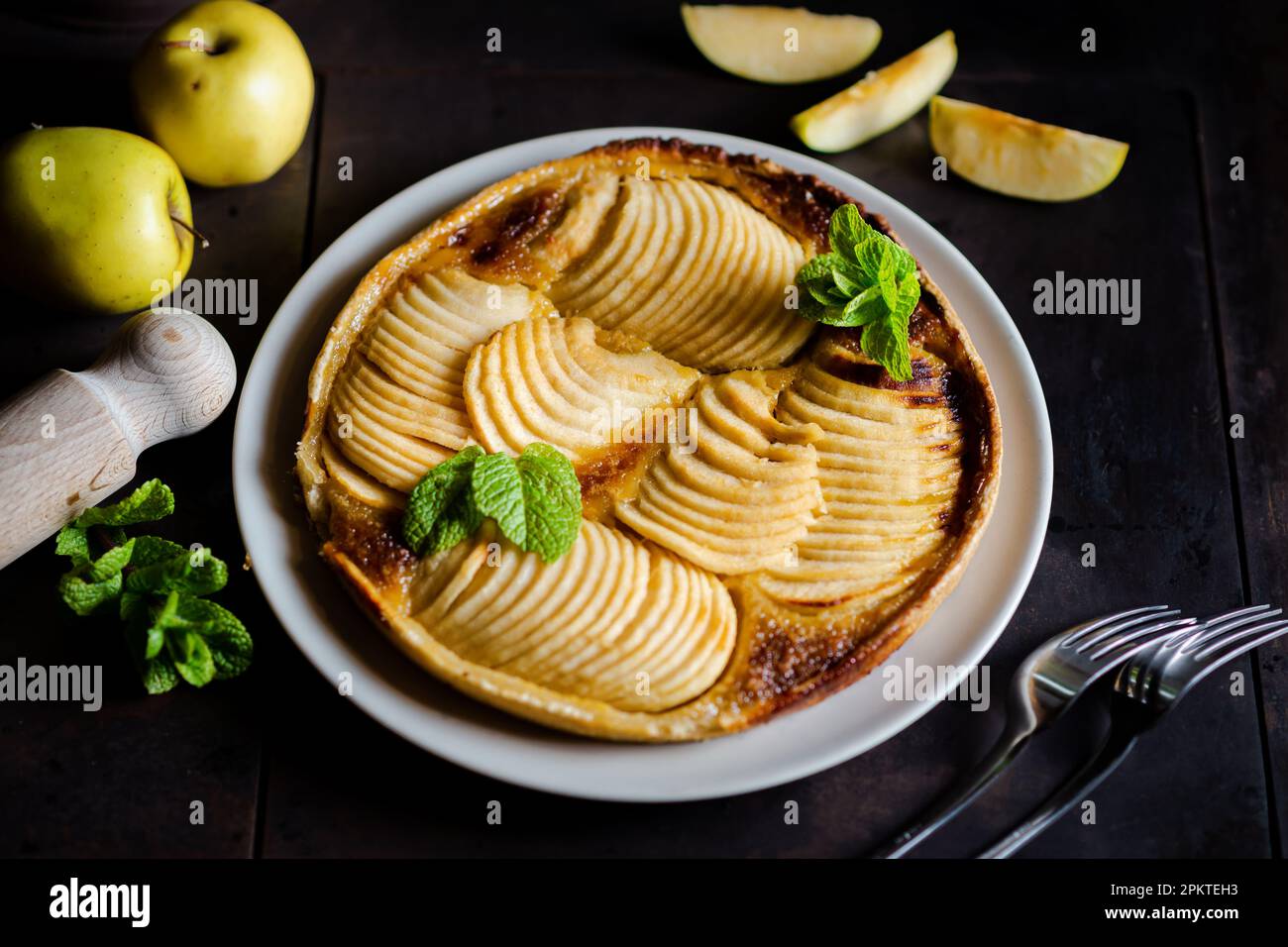 apfelkuchen: Versuchung auf schwarzem Hintergrund. Traditioneller offener Kuchen mit dünnen Äpfelstücken, dekoriert mit Minzblättern. Stockfoto