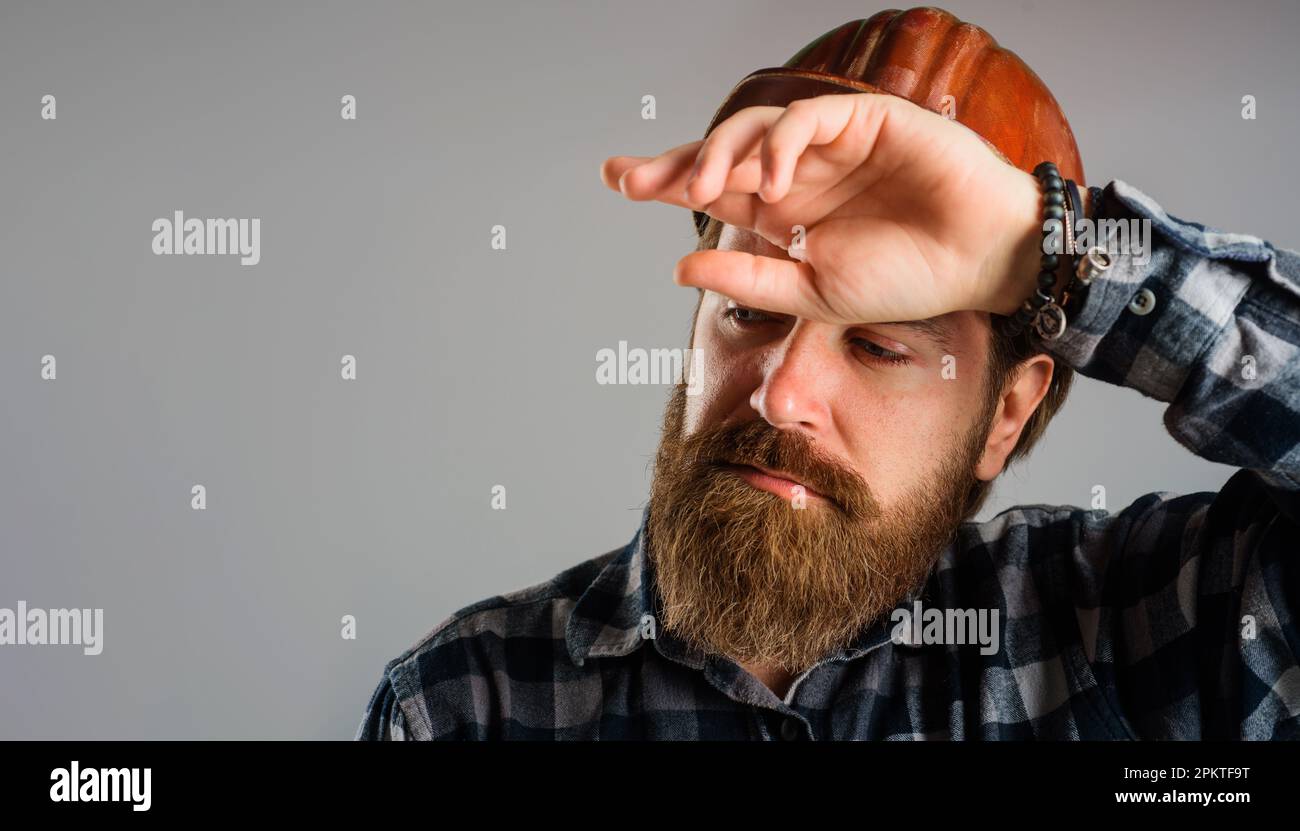 Der müde Baumeister mit Schutzhelm wischte Schweiß von der Stirn ab. Gebäude, Industrie, Technologie. Harte Arbeit auf der Baustelle. Schwerer Beruf. Mechanische Schnecke Stockfoto