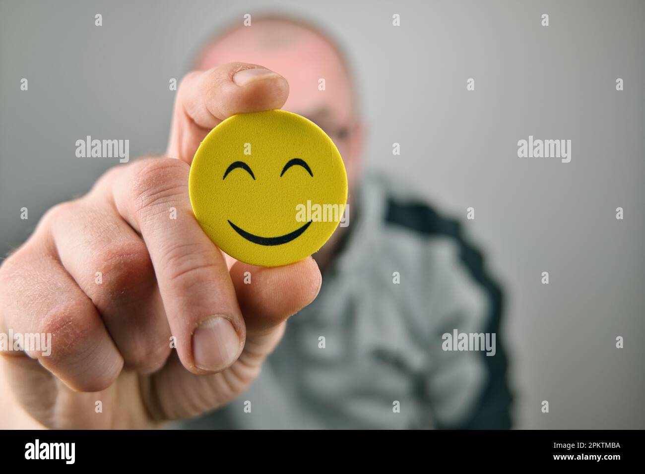 Person, die ein gelbes Smiley-Gesicht Emoji vor seinem Gesicht hält Stockfoto