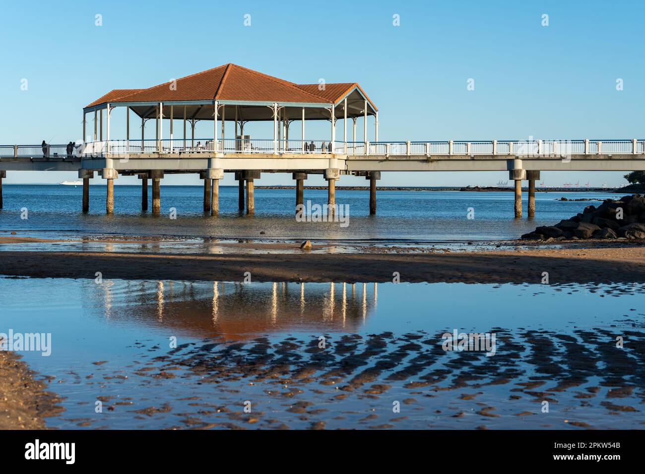 Rotunda auf Redcliffe Jetty spiegelt sich in einem Wasserbecken bei Ebbe, mit Blick über Moreton Bay zum Hafen von Brisbane am Horizont. Stockfoto