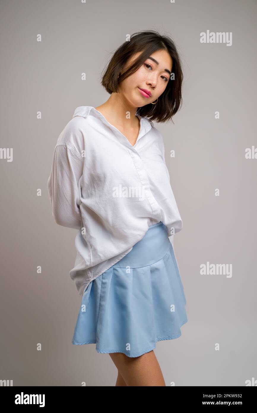 3/4 Body Portrait einer jungen asiatischen Frau mit einem kurzen blauen Rock und einem weißen Langarmshirt | Weißer Hintergrund Stockfoto
