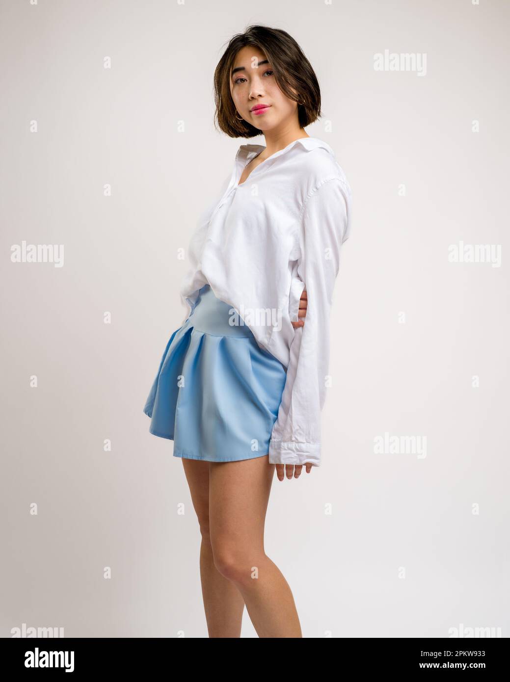 3/4 Body Portrait einer jungen asiatischen Frau mit einem kurzen blauen Rock und einem weißen Langarmshirt | Weißer Hintergrund Stockfoto