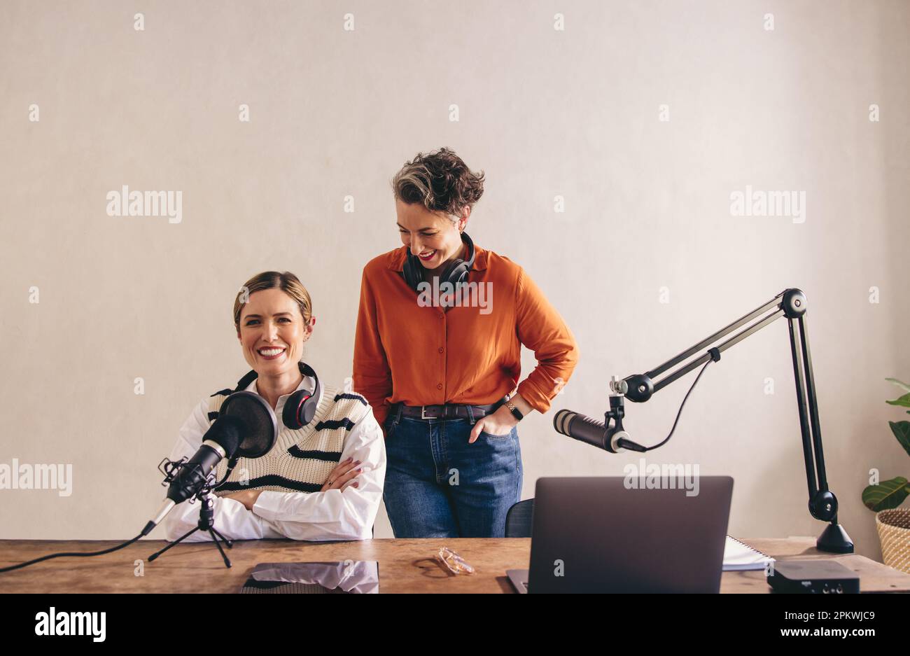 Fröhliche Podcaster, die mit Headsets um den Hals lachen. Zwei Frauen, die gemeinsam eine Audioübertragung in einem Heimstudio moderieren. Weibliche Inhaltscreato Stockfoto
