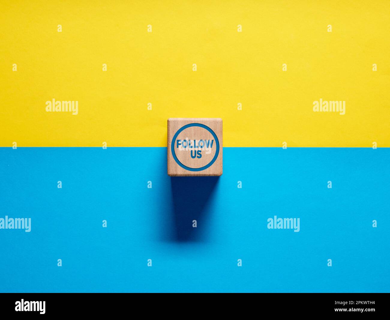 Das Wort folgt uns auf einem hölzernen Würfel auf blauem und gelbem Hintergrund. Konzept für Follower in sozialen Medien oder im Internet. Stockfoto