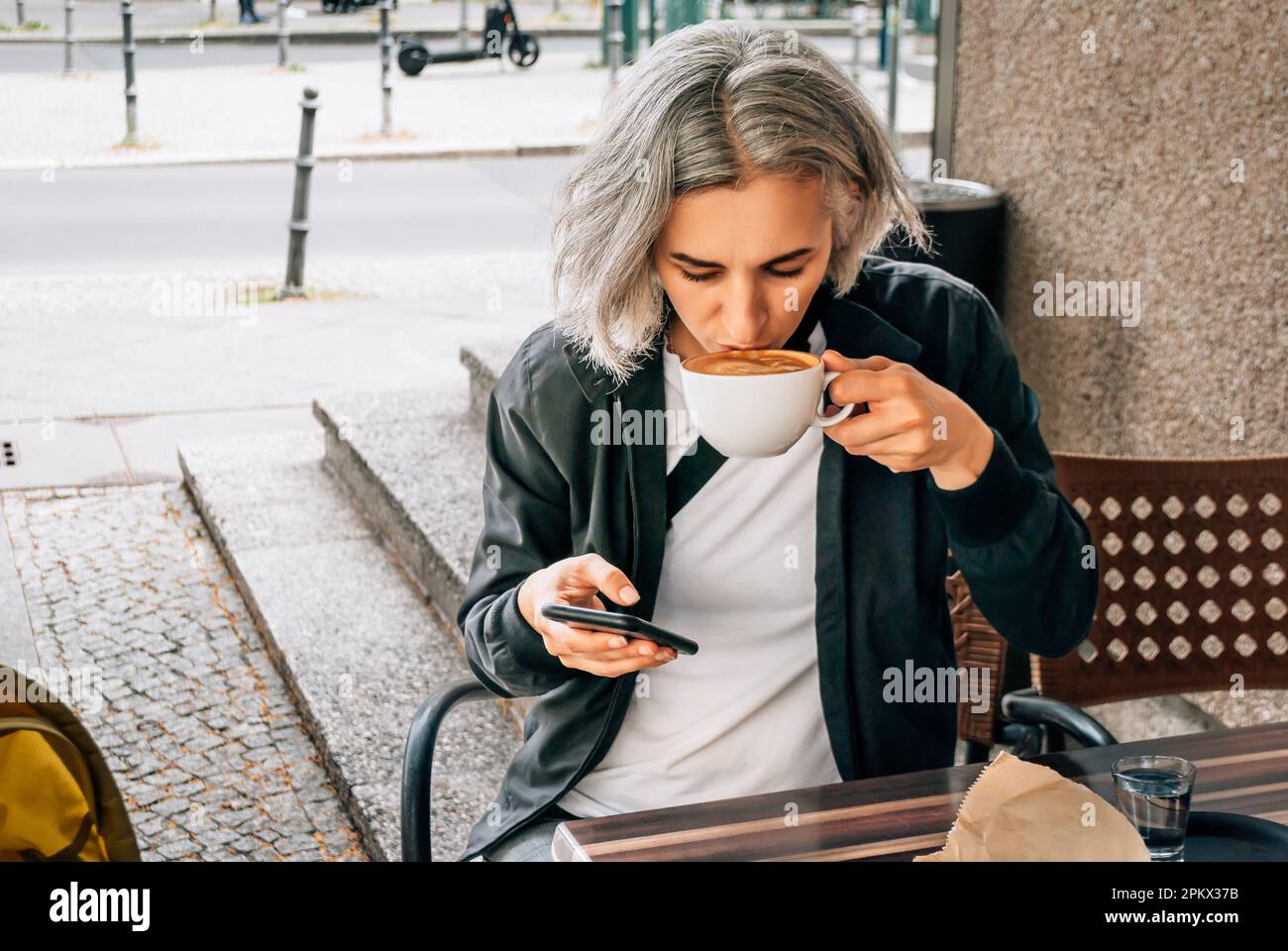 Eine Frau trinkt Kaffee und telefoniert am Tisch des Cafés im Freien Stockfoto