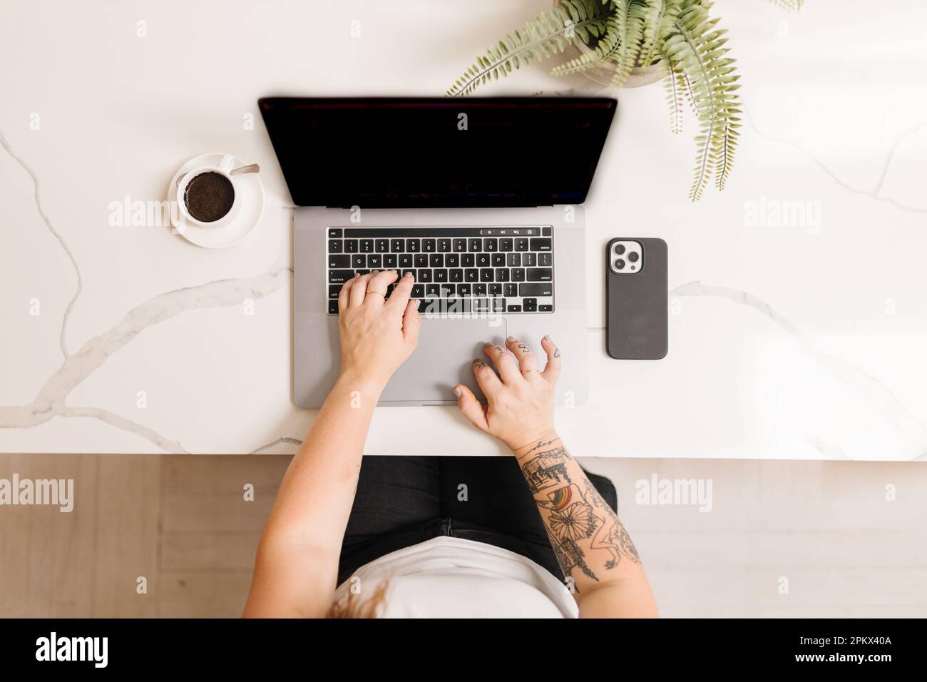 Tätowierte Arme, die auf einem Computer mit Espresso und Telefon tippen Stockfoto
