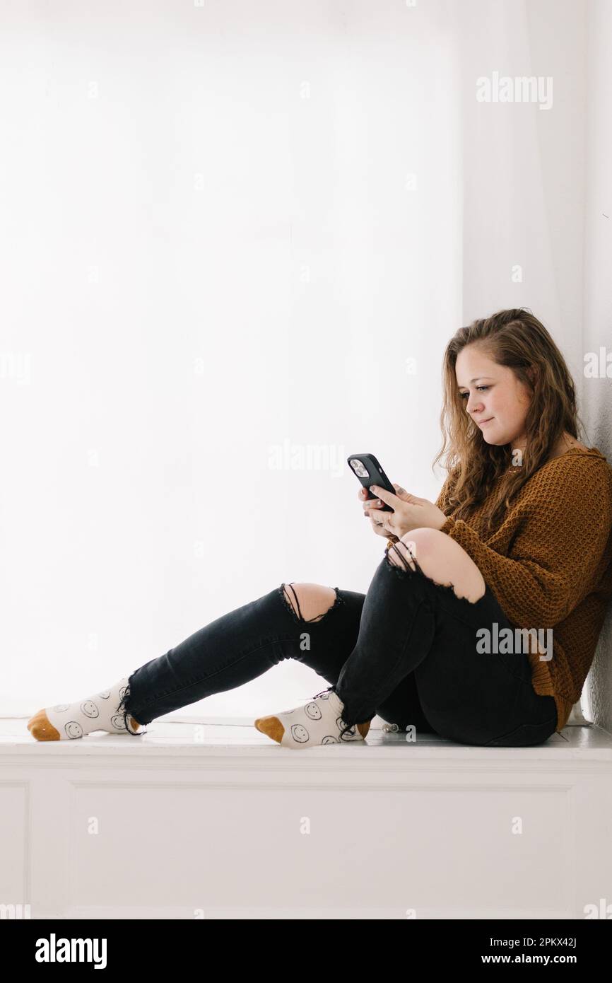 Frau, die im weißen Winkel sitzt und auf ein Smartphone schaut Stockfoto