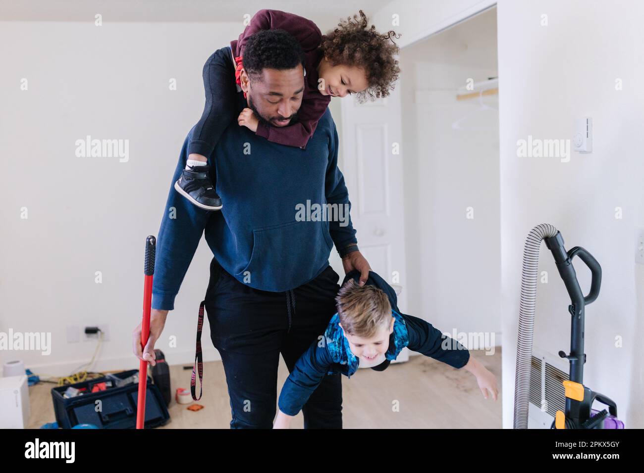 Schwarzer Dad hält zwei Kinder, während er das Haus putzt Stockfoto