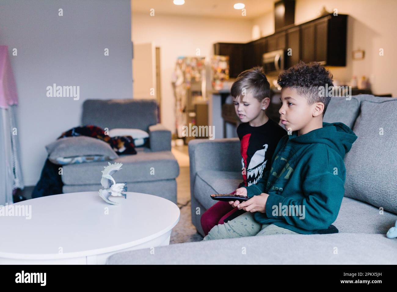 Multirassische Brüder, die mit der Fernbedienung auf einer grauen Couch sitzen Stockfoto