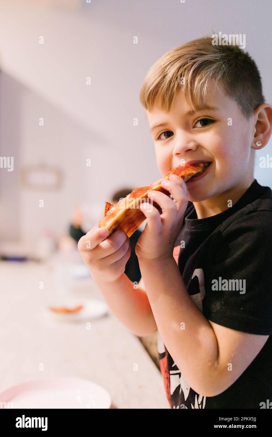 Ein lächelnder weißer Junge, der Pizzabissen nimmt und in die Kamera starrt Stockfoto