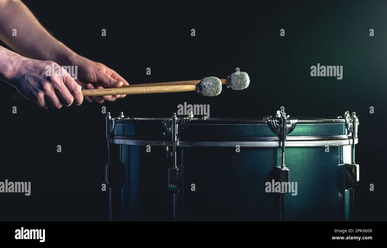 Ein Mann spielt ein musikalisches Schlaginstrument mit Stöcken auf dunklem Hintergrund. Stockfoto