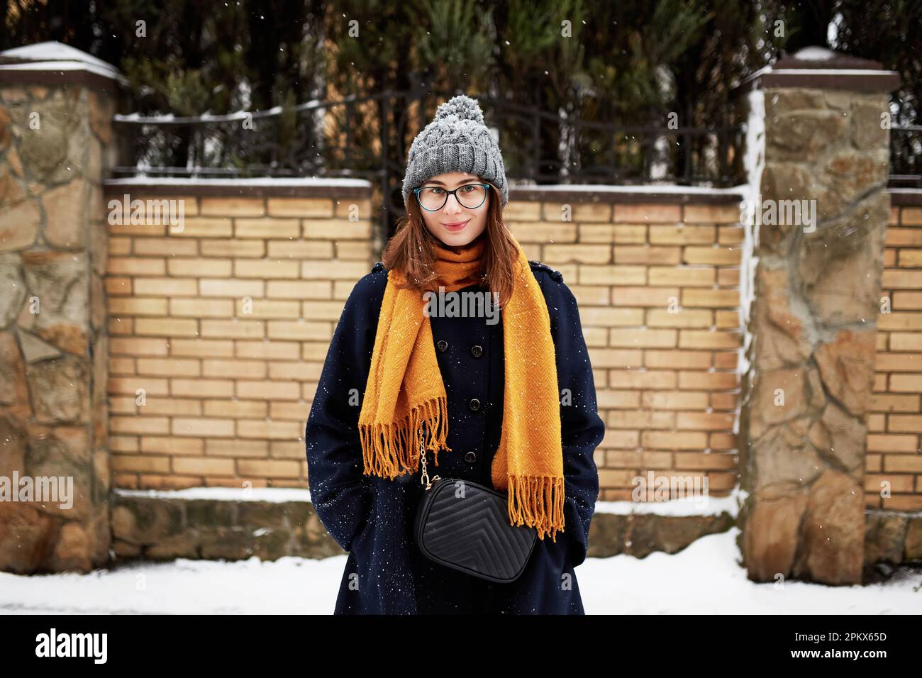 Eine Frau mit gelbem Schal und blauem Mantel mitten in einer verschneiten Straße Stockfoto