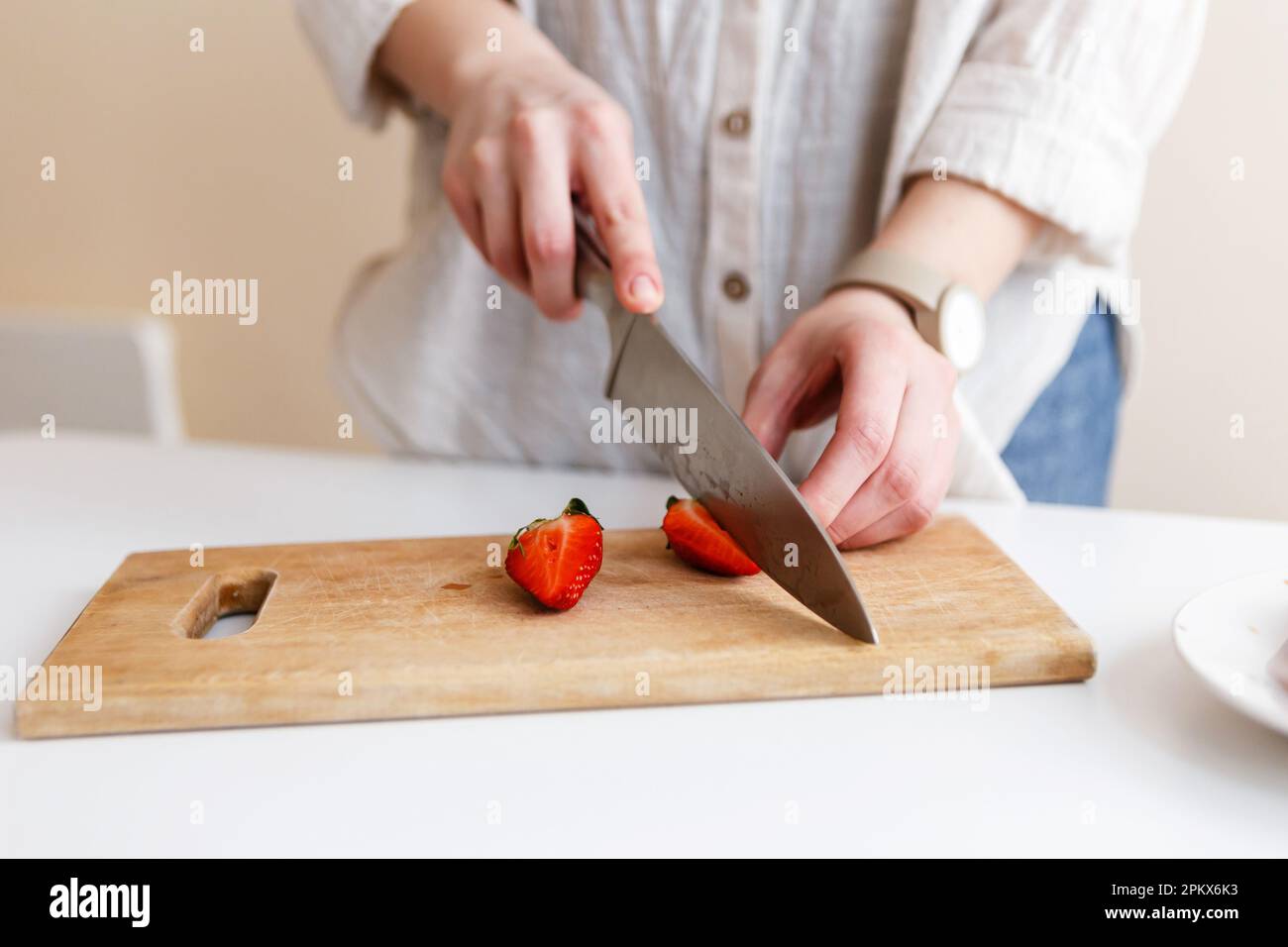 Eine Köchin schneidet rote, frische Erdbeeren mit einem Messer in der Küche Stockfoto