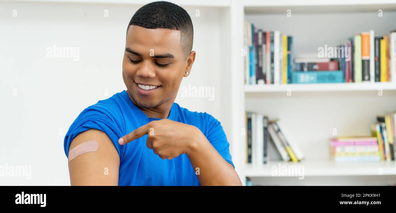 Hispanischer junger Erwachsener, der nach Impfung gegen Covid 19 in der Arztpraxis auf Gips zeigt Stockfoto