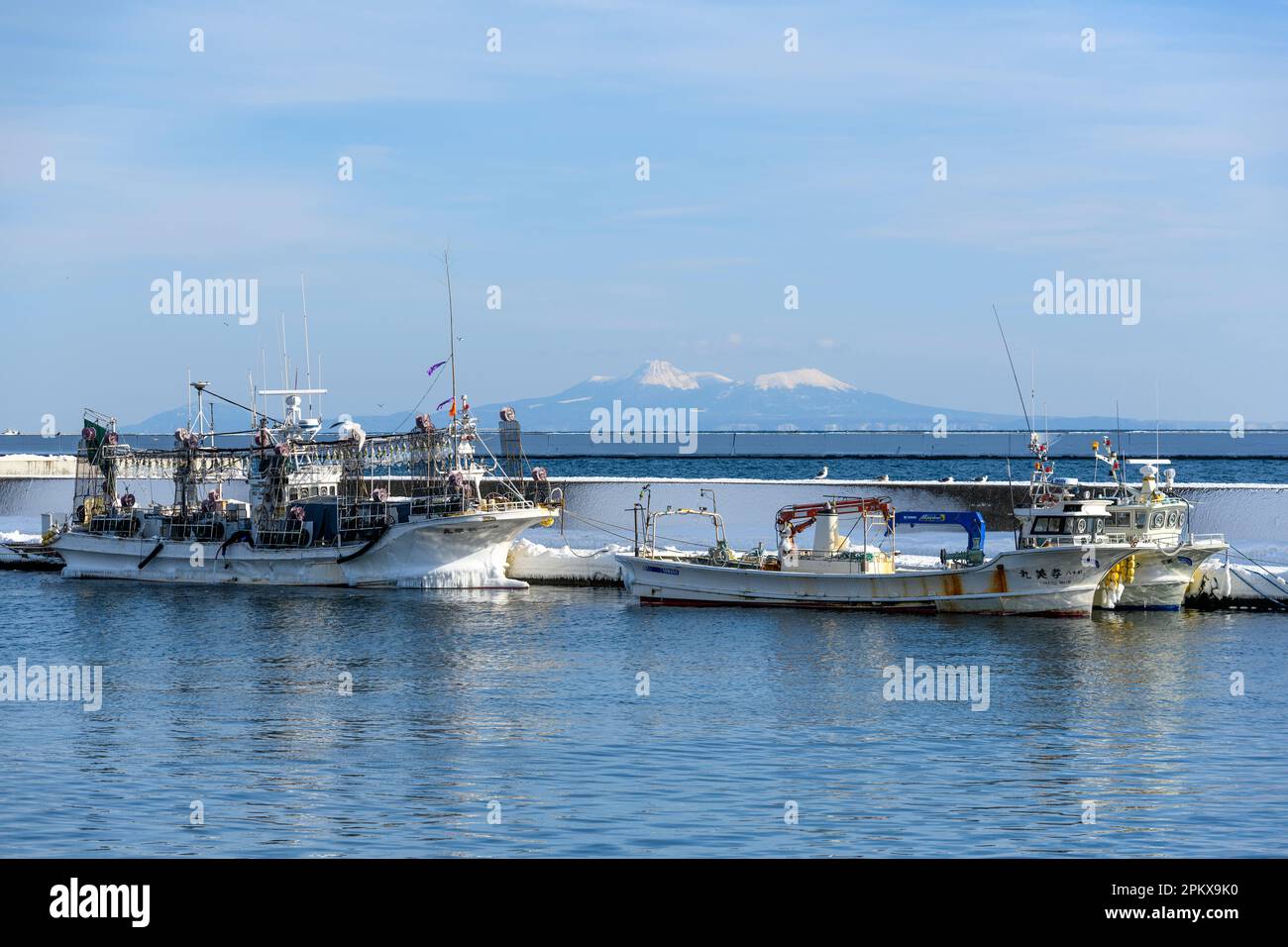 Japanische Fischerboote im Hafen von Rausu, Hokkaido, Japan. Die Insel Kunashir liegt im fernen Hintergrund. Stockfoto