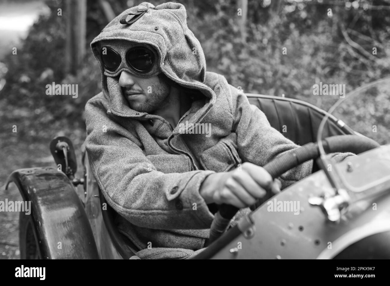 Road Trip mit einem Oldtimer Austin 7 Mann mit Brille Vintage Look Fahren auf einer Landstraße in England. Stockfoto