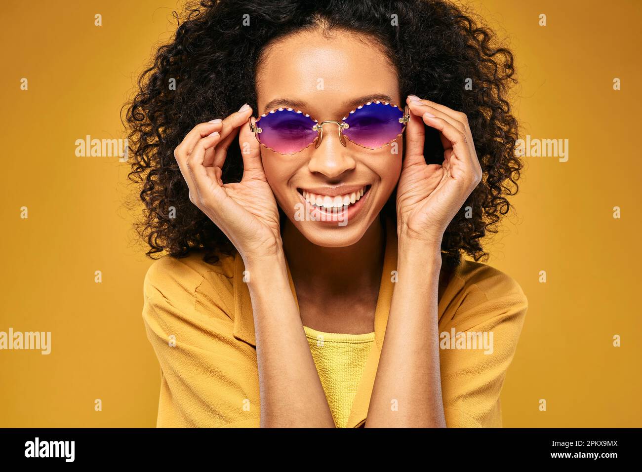 Wunderschöne afroamerikanische Frau mit stilvoller Sonnenbrille, Nahaufnahme auf gelbem Hintergrund Stockfoto