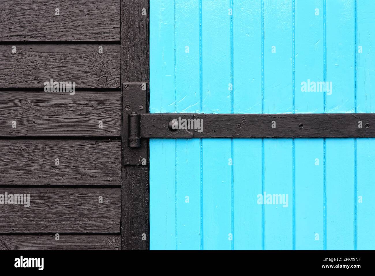 Ein zweidimensionales Design durch eine blau lackierte Holztür mit schwarzem Scharnier und dunkler Holzverkleidung Stockfoto