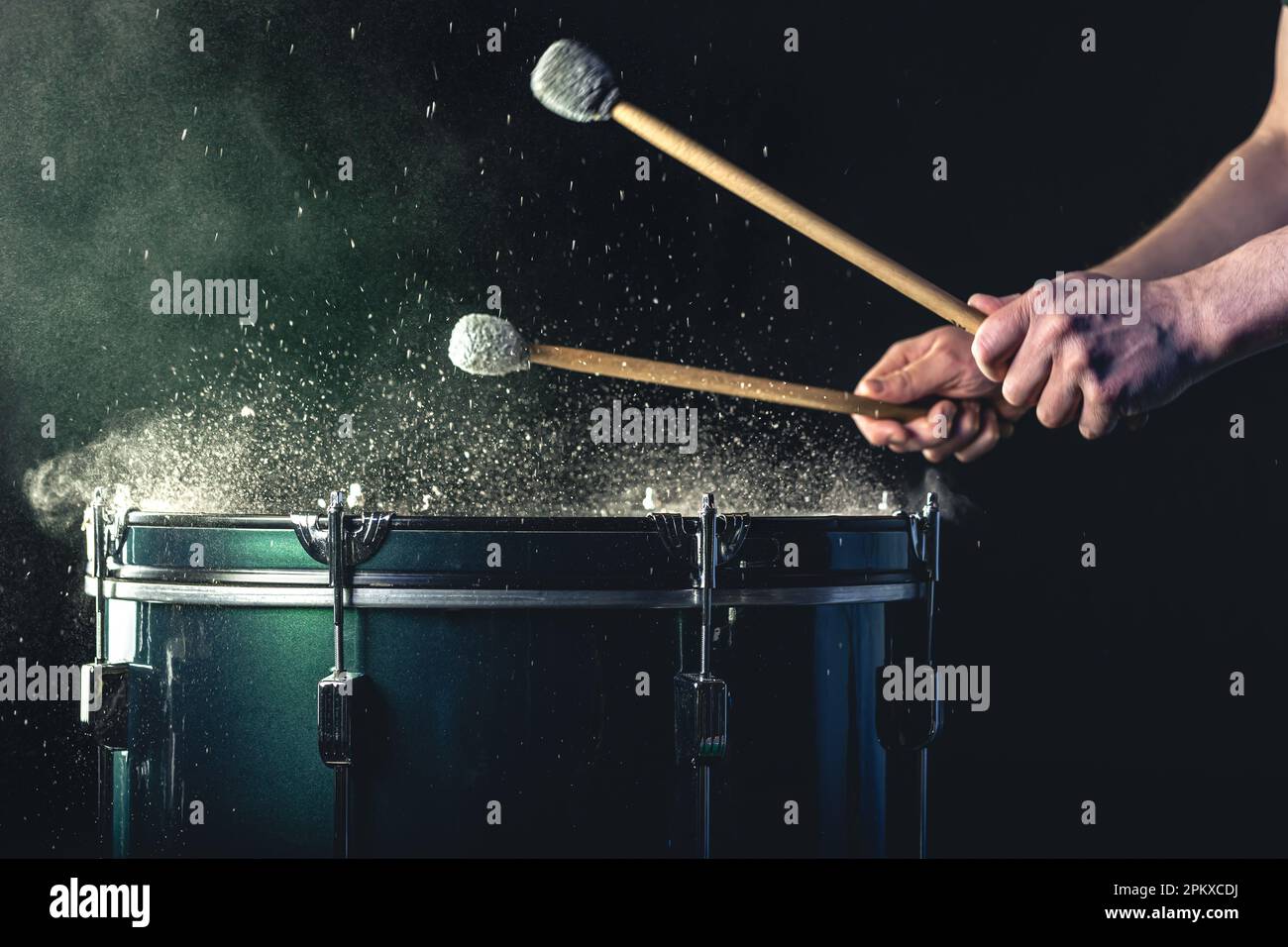 Ein Mann spielt ein musikalisches Schlaginstrument mit Stöcken auf dunklem Hintergrund. Stockfoto