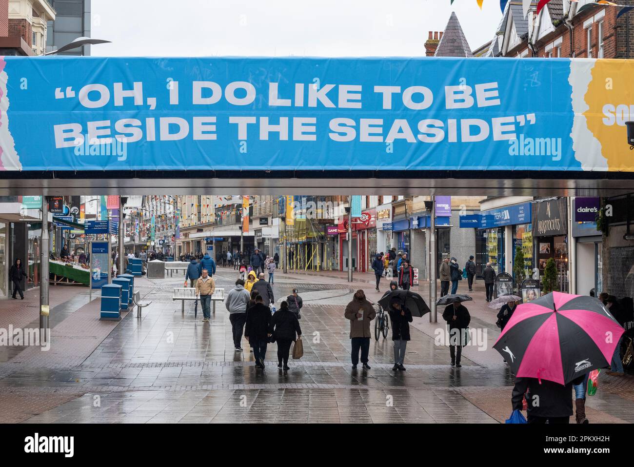 Southend on Sea, Essex, Großbritannien. 10. April 2023. Der Feiertag in Southend auf See hat den ganzen Morgen Regen gesehen. Ein paar Leute sind draußen im kämpfenden Einkaufsviertel der High Street. Die Sicherheitsmaßnahmen wurden eingerichtet, um eine traditionelle Zusammenkunft von Motorrädern zu verhindern, die den Fischern an der Küste sonst geholfen hätte, Geschäfte zu machen. Leute in der High Street mit Schirmen, die unter der Eisenbahnbrücke vorbeifahren mit „Oh, ich bin gerne am Meer“ Stockfoto