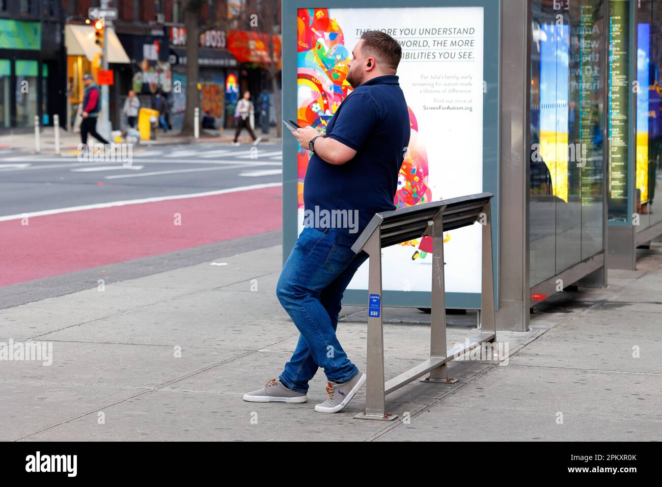Eine Person, die sich an einer neigenden Bar oder einer neigenden Bank an einer Bushaltestelle in Manhattan in New York City ruht. Feindliche Architektur gegen Sitzen und herumlungern. Stockfoto