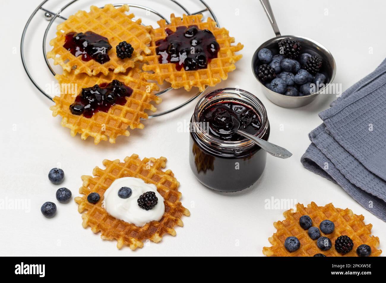 Ein Glas Marmelade. Waffeln mit Marmelade und Beeren auf dem Tisch. Beeren in einer Schüssel. Flach verlegt. Weißer Hintergrund. Stockfoto