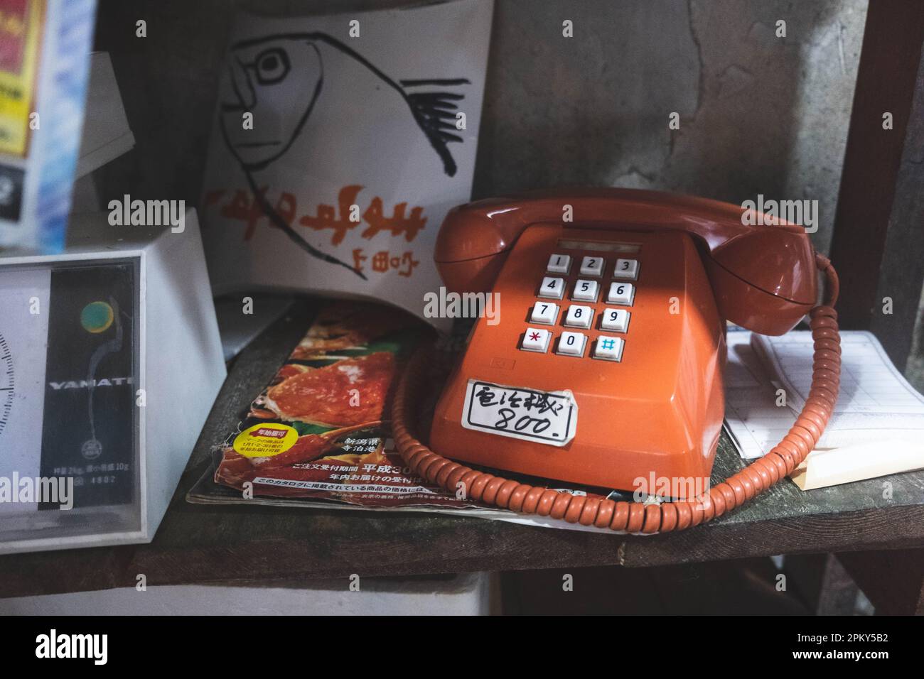 Rotes Vintage-Telefon mit japanischem Aufkleber und japanischen Zeitschriften auf dem Regal Stockfoto