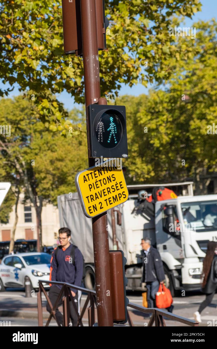 Grüne Fußgängerampel mit gelbem Schild „ACHTUNG PIETONS TRVERSEE EN 2 TEMPS“ Stockfoto