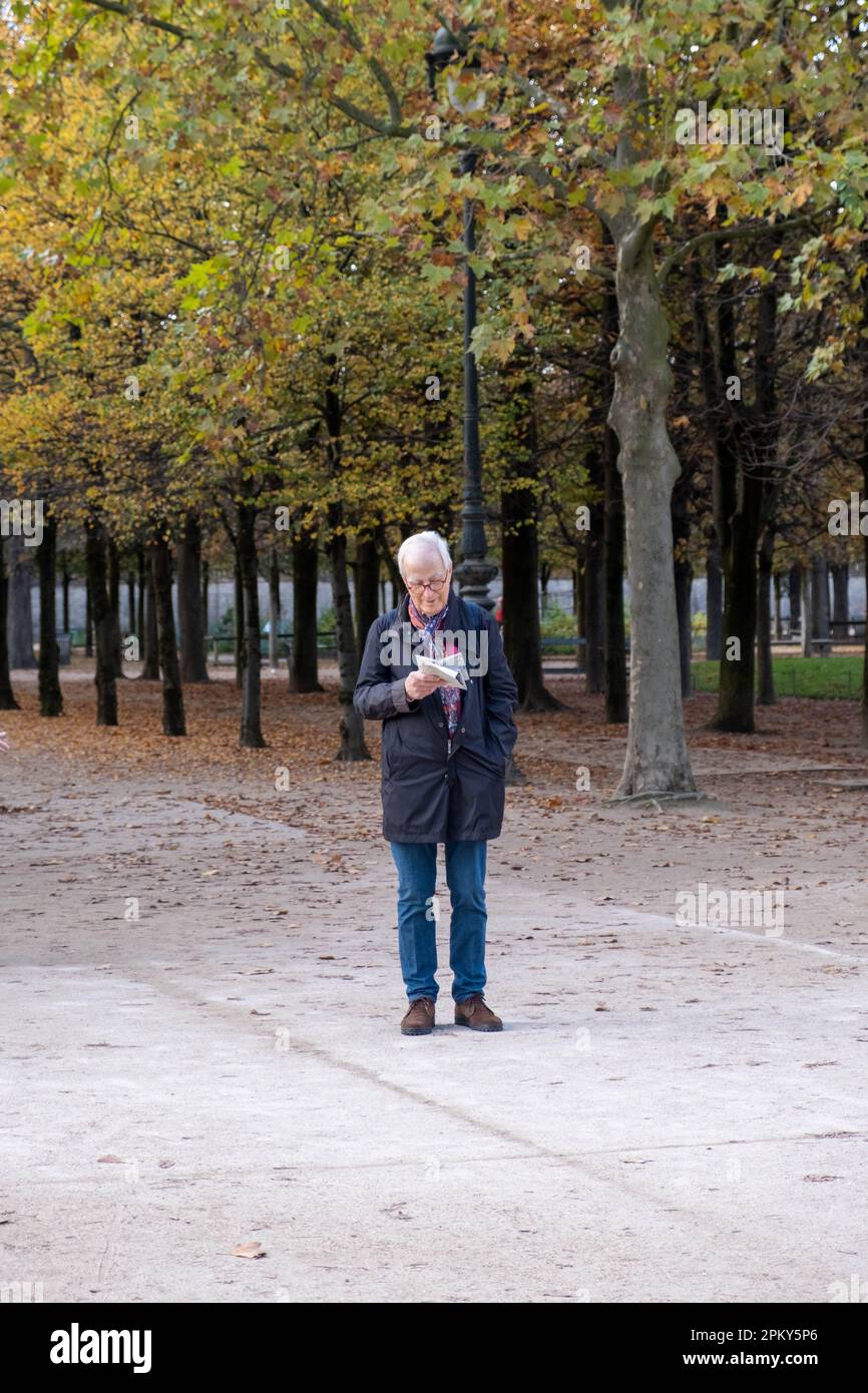 Senior Gentleman in Coat betrachtet den Pariser Garten mit Bäumen im Hintergrund Stockfoto