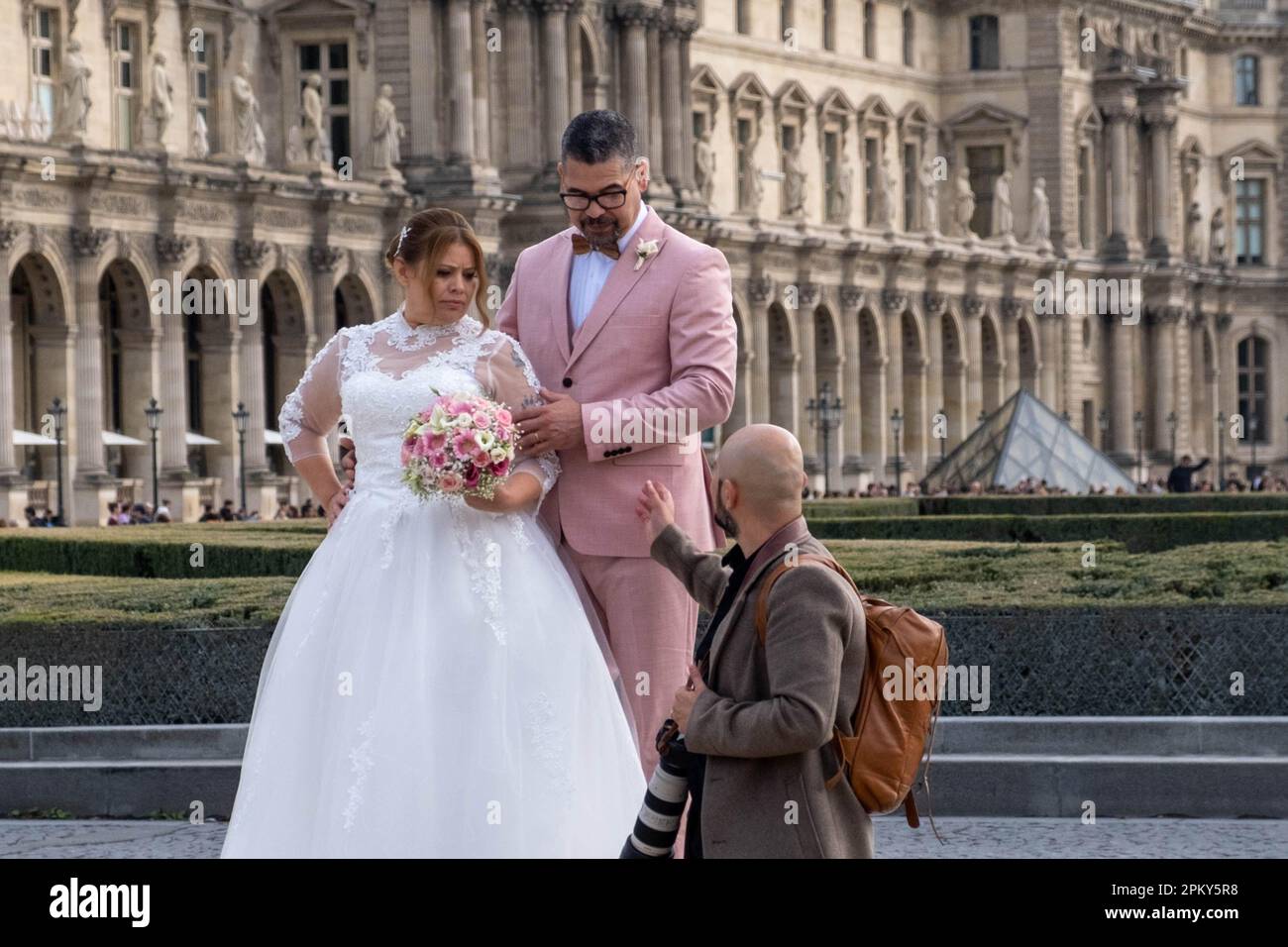 Stilvolles spanisches Paar in rosafarbener Hochzeitskleidung posiert für ein romantisches Fotoshooting im Louvre, Paris Stockfoto
