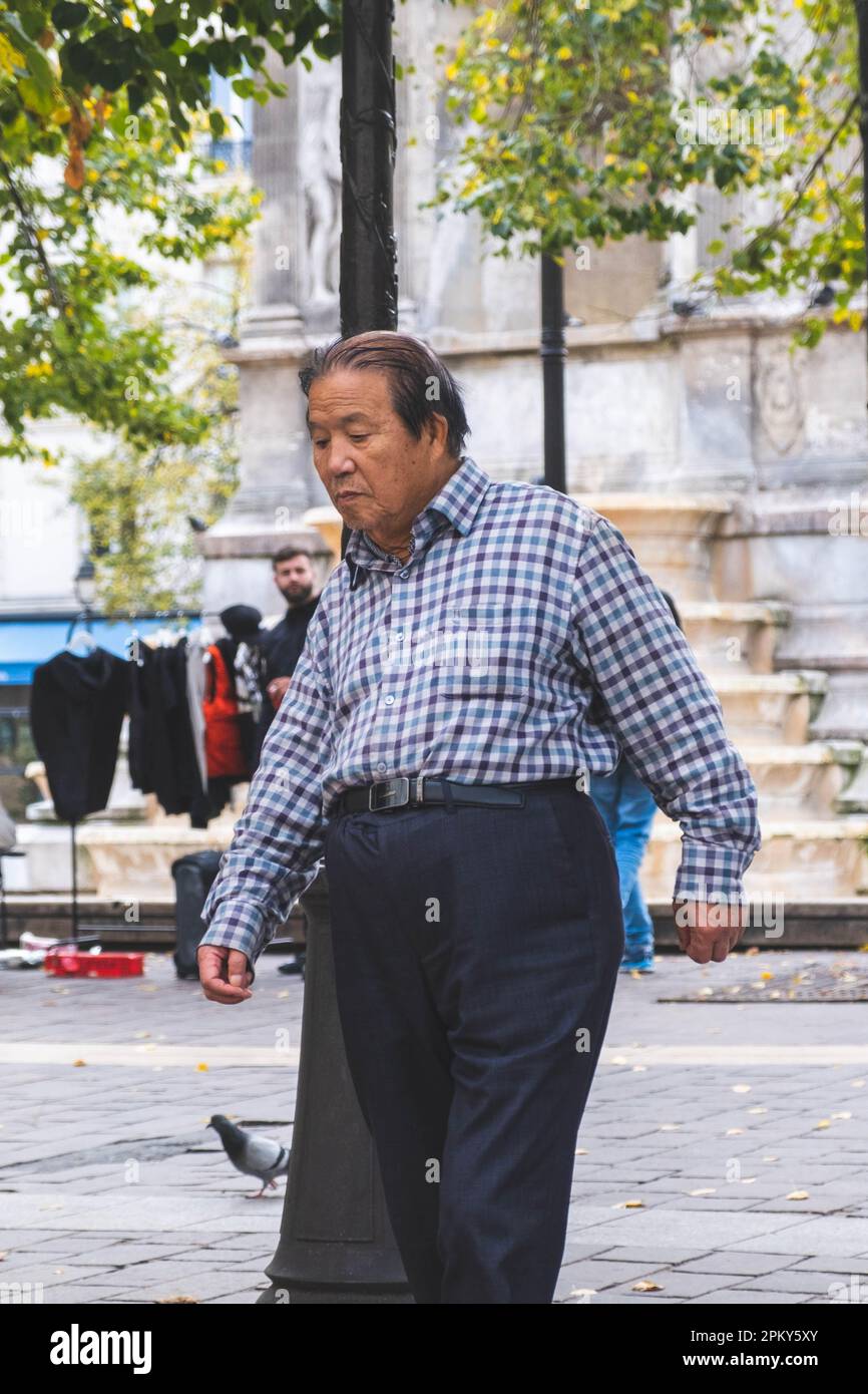 Ein älterer Chinese schlendert durch die bezaubernden Straßen von Paris und bewundert die Sehenswürdigkeiten und Klänge der Stadt der Liebe Stockfoto